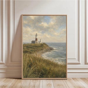 May include: A framed wall art print depicting a coastal landscape with a lighthouse standing on a grassy cliff overlooking the ocean. The scene features a white and red lighthouse, rolling green hills, tall grasses, and a cloudy blue sky.