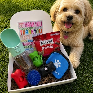 May include: A white gift box containing a mint green portable water bottle, a red Milk-Bone mini's treat bag, a blue spiky ball, a blue pouch with a white paw print, and three bone-shaped waste bag dispensers in red, green, and black.