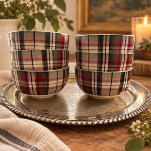 May include: A set of six round ceramic bowls featuring a classic plaid pattern in shades of red, dark green, black, and cream. The bowls are stacked in two columns of three on a round, silver-toned metal tray with an ornate, embossed edge.