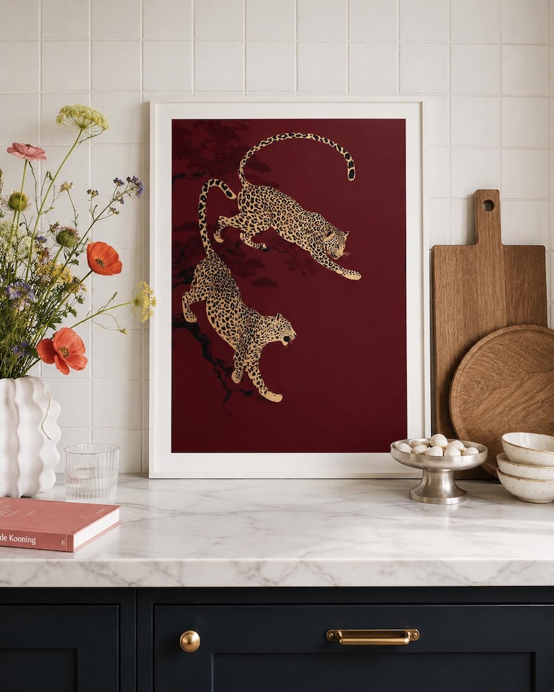 May include: A rectangular wall art print in a white frame featuring two leopards with black spots on a deep burgundy background. The leopards are depicted in motion, positioned as if climbing or leaping among dark, silhouetted tree branches.
