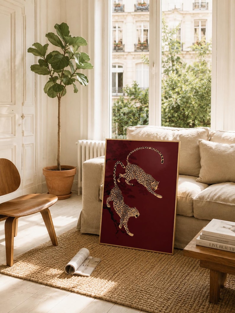 May include: A rectangular framed wall art piece featuring two gold-colored leopards depicted in a dynamic, leaping pose against a deep, solid burgundy red background. The leopards are illustrated with detailed black spots and are positioned diagonally.