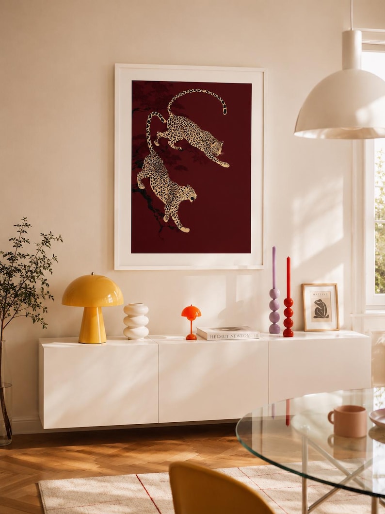 May include: A framed vertical wall art print featuring two leopards with spotted fur climbing on dark branches against a deep burgundy background. The artwork is displayed in a white frame, showcasing a detailed illustration of the wild cats.
