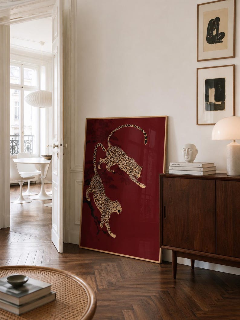 May include: A large rectangular framed wall art piece featuring a deep red background with two illustrated leopards climbing on dark tree branches. The leopards are depicted with gold and black spotted fur, positioned one above the other.