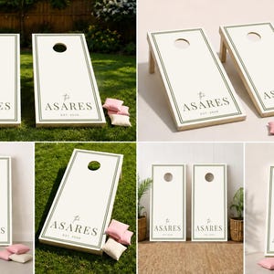 Könnte beinhalten: Ein Set aus zwei weißen Cornhole-Boards mit dunkelgrünen Randlinien und dem in Dunkelgrün aufgedruckten Text "The ASARES EST. 2024". Die Boards haben ein kreisförmiges Loch im oberen Bereich und werden von kleinen hellrosa und weißen Sitzsäcken begleitet.