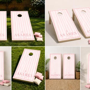 Könnte beinhalten: Ein Set aus zwei Cornhole-Boards mit einem hellrosa-weißen vertikalen Streifenmuster. Jedes Board hat ein kreisförmiges Loch im oberen Bereich und den in Rosa aufgedruckten Schriftzug ASARES im unteren Bereich. Das Set enthält kleine Sitzsäcke.