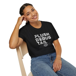 May include: A black short-sleeved t-shirt featuring white text that reads FLUSH DEBUG TAIL in a digital glitch font style. Below the text is a white wireframe graphic of a globe sitting on a grid surface. The shirt has a crew neckline.