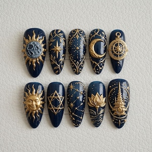 May include: A set of ten almond-shaped press-on nails in a deep navy blue base color. Each nail features intricate, raised gold-toned relief designs including a sun, moon, stars, lotus flower, geometric patterns, and a celestial temple structure.