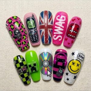 May include: Ten press-on nails featuring diverse designs including a pink leopard print with a silver skull, a flip phone, a Union Jack flag, the word SWAG, a red monster, a green checkerboard, a creeper face, a CD, headphones, and a smiley face.