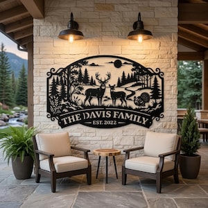 May include: A black metal wall sign featuring a laser-cut forest scene with a deer, a doe, and a turkey. The text reads THE DAVIS FAMILY EST. 2022. The sign has an arched top and decorative scrollwork on the sides, mounted on a stone wall.