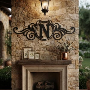 May include: A black metal wall sign featuring a central letter N surrounded by decorative scrollwork. The sign is mounted on a stone wall above a fireplace mantel, which holds three framed botanical prints and a copper vase with greenery.