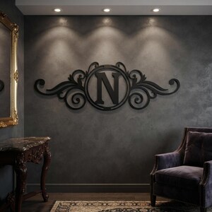 May include: A black wall-mounted sign featuring a central circular frame containing the capital letter N, flanked by symmetrical, intricate scrollwork and leaf-like flourishes extending horizontally across the dark grey wall surface.