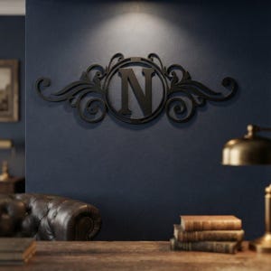 May include: A black wall-mounted letter N monogram sign featuring a circular frame surrounded by decorative scrollwork and flourishes. The piece is constructed with a solid matte finish and is centred on a dark blue wall surface.