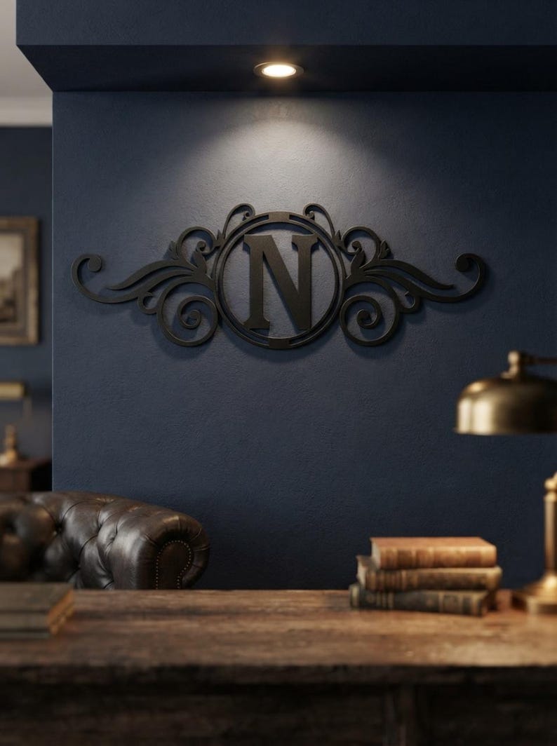 May include: A black wall-mounted letter N monogram sign featuring a circular frame surrounded by decorative scrollwork and flourishes. The piece is constructed with a solid matte finish and is centred on a dark blue wall surface.