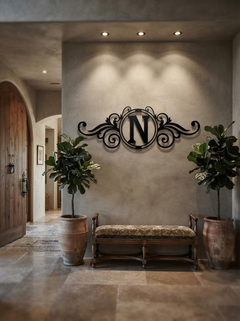 May include: A black metal wall sign featuring a central circular frame enclosing the capital letter N, flanked by symmetrical decorative scrollwork and flourishes. The piece is mounted on a wall above a bench, displaying a dark finish.