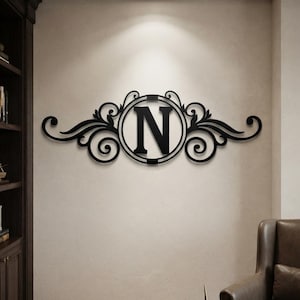 May include: A black wall-mounted sign featuring a central circular frame containing the capital letter N, flanked by symmetrical decorative scrollwork and leaf-like flourishes extending horizontally on both sides of the central letter.