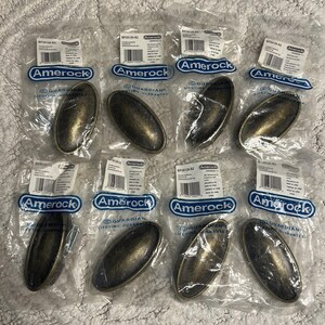 May include: Eight oval-shaped Amerock cabinet pulls with a dark, weathered bronze finish, each individually sealed in a clear plastic bag with a white label featuring a barcode and the text Amerock Guardian Lifetime Guarantee.