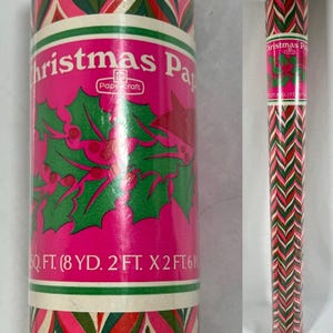 May include: A roll of wrapping paper featuring a bright pink background with green holly leaves and red berries. The label reads Christmas Paper, Papercraft, and 50 SQ. FT. (8 YD. 2 FT. X 2 FT. 6 IN.). The pattern includes a chevron design.