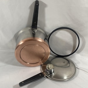 May include: A stainless steel pressure cooker with a copper-colored base and a black handle. The set includes a circular lid with a black rubber gasket and an integrated pressure gauge dial, featuring a long black handle attached to the lid.