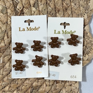 May include: Two white rectangular display cards labeled La Mode, each holding four brown teddy bear-shaped buttons. The buttons are arranged in two rows of two on each card. The cards feature the text La Mode and the number 684 printed on them.