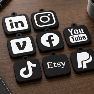 May include: A collection of eight square black tags with white social media and platform logos, including LinkedIn, Instagram, Vimeo, Facebook, YouTube, TikTok, Etsy, and PayPal. Each tag features a small circular hole at the top for attachment.