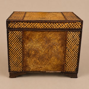 May include: A rectangular storage chest featuring a woven dark brown bamboo frame and side panels. The central front panel is made of a textured, mottled golden-brown material embossed with a detailed design of three palm trees.