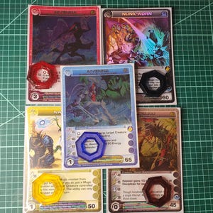 May include: Five rectangular trading cards featuring fantasy illustrations and text, including Nivenna, Nunk'worn, Aivenna, and Kepiaan. Each card is paired with a translucent hexagonal plastic token in red, black, blue, yellow, or brown.