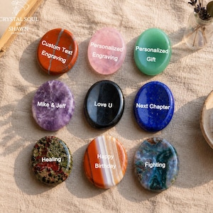 Puede incluir: Nueve piedras pulidas de forma ovalada en varios colores y patrones, cada una con texto grabado en blanco. Las piedras incluyen variedades roja, rosa, verde, morada, negra, azul, verde moteada, rayada naranja y azul verdosa con inscripciones.