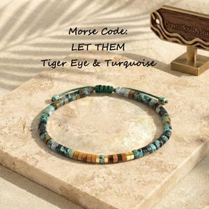 May include: A Morse code bracelet featuring small, cylindrical beads in shades of turquoise, brown, and gold. The text above the bracelet reads: Morse Code: LET THEM Tiger Eye & Turquoise. A wooden sign with the text Crystal Soul By Shawn is visible.