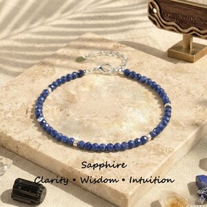 Può includere: Un braccialetto di perline composto da piccole perle di zaffiro blu scuro sfaccettate alternate a distanziatori in metallo color argento. Il braccialetto include una chiusura a moschettone color argento e una catenella di estensione. Il testo recita Sapphire Clarity Wisdom Intuition.