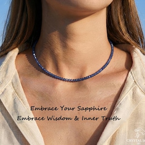 May include: A delicate necklace featuring small, faceted blue sapphire beads arranged in a single strand. The text "Embrace Your Sapphire" and "Embrace Wisdom & Inner Truth" is printed below the necklace, along with a logo for Crystal Soul by Shawn.