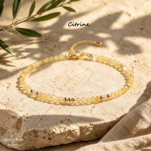 May include: A delicate bracelet featuring small, faceted yellow citrine beads interspersed with polished gold-tone metal spheres. The piece includes a gold-tone metal clasp and chain extender. The text Citrine is visible above the bracelet.