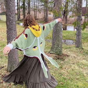 Peut inclure: Un cardigan en crochet conçu pour ressembler à un papillon de nuit avec un corps vert clair, des bordures marron foncé et une capuche jaune. Le dos présente de grands panneaux en forme d'ailes avec des motifs d'ocelles jaunes, noirs et rouges.