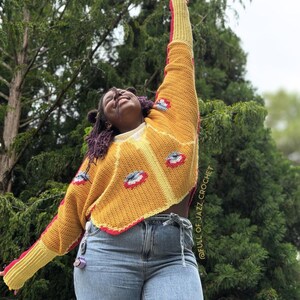 May include: A long-sleeved crochet sweater in mustard yellow with red and white eye-shaped motifs. The sweater features a ribbed yellow cuff, a scalloped hem, and the text @FULL_OF_JAZZ_CROCHET printed vertically along the side of the garment.