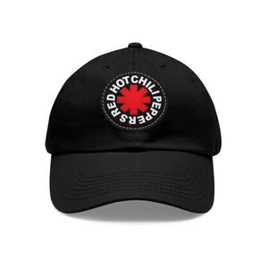 Peut inclure: Casquette de baseball noire avec un écusson circulaire portant l'inscription "RED HOT CHILI PEPPERS" autour d'une étoile rouge. La casquette a une visière incurvée et une sangle réglable.