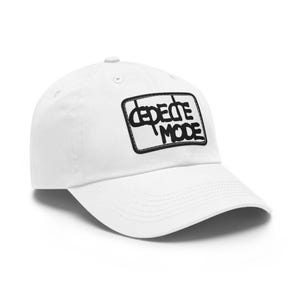 May include: A white baseball cap featuring a rectangular black and white patch on the front panel. The patch displays the text Depeche Mode in a stylised, bold black font. The cap has a curved brim, a button on top, and stitched eyelets.