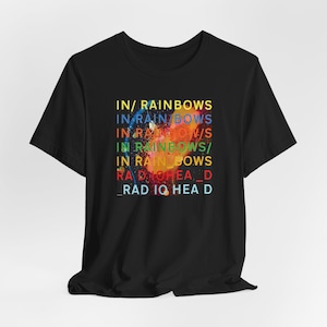 以下が含まれることがあります： 黒いTシャツ。カラフルなスプラッターデザインで「IN/ RAINBOWS」の文字がプリントされています。テキストは縦に積み重ねられ、バンド名「RADIOHEAD」が含まれています。Tシャツは、クラシックなクルーネックです。