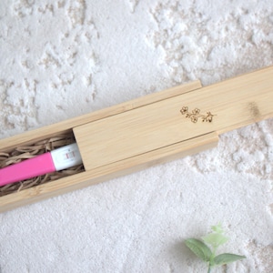 Könnte beinhalten: Ein rosa Schwangerschaftstest in einer natürlichen Bambusbox mit Schiebedeckel. Der Deckel ist mit einem floralen Design verziert. Die Box ist mit geschreddertem Papier ausgekleidet.