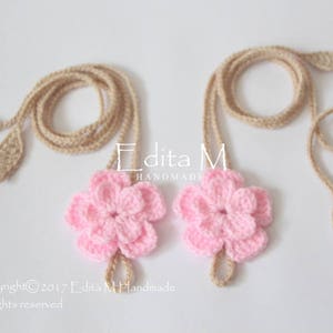 May include: Two handmade crochet barefoot sandals. Each sandal features a pink flower with a beige cord and leaf accents. The sandals are displayed on a white surface. The text "Edita M Handmade" is visible.
