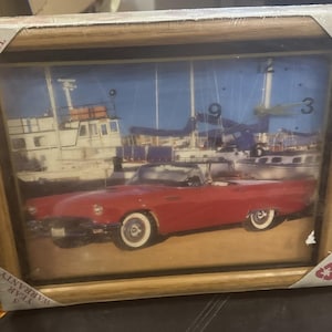 May include: A rectangular wall clock with a light wood frame featuring a printed image of a red vintage convertible car parked in front of a white boat at a marina. The clock face includes numbers 3, 6, 9, and 12, with text stating Made in the U.S.A. and World Clock.