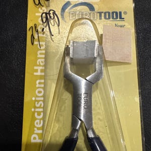 May include: A pair of silver-colored metal pliers with dark blue handles, encased in clear plastic packaging on a yellow card. The tool is labeled EURO TOOL and the packaging features the text Precision Hand Tools and EUROTOOL.