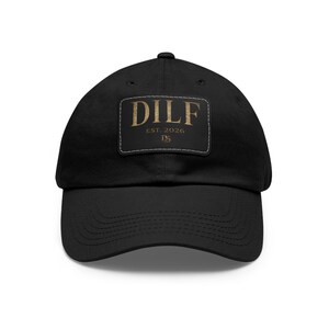 May include: Black baseball cap with a curved brim. The cap features a rectangular patch with the word "DILF" in gold lettering, along with "EST. 2026" and the initials "FS". The cap is made of a soft fabric.