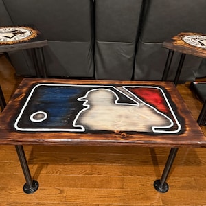 Può includere: Un tavolino in legno e due sgabelli abbinati. Il tavolo presenta un design a silhouette di giocatore di baseball con accenti blu e rossi. Gli sgabelli hanno un logo dei Blue Jays di Toronto. Tutti i pezzi hanno gambe in metallo nero.