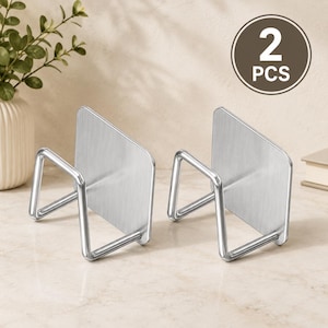 May include: A set of two silver-colored metal adhesive wall hooks, each featuring a flat rectangular mounting plate and a protruding U-shaped wire support arm. The image includes a circular graphic in the top right corner with the text 2 PCS.