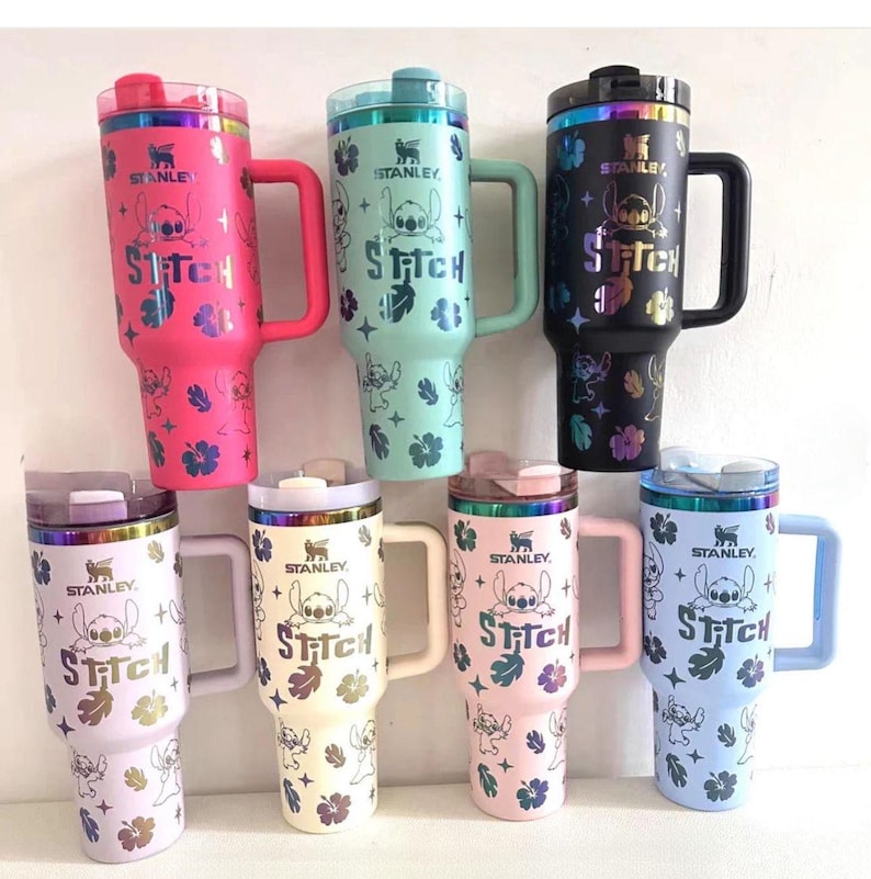 May include: Seven Stanley tumblers with handles and lids, each featuring a holographic Stitch character print, hibiscus flowers, and the text Stitch. The tumblers come in pink, mint green, black, light purple, cream, light pink, and light blue colors.
