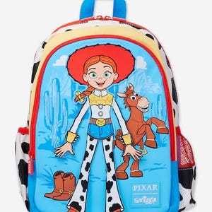 May include: A blue backpack featuring a graphic of Jessie the cowgirl and Bullseye the horse from Toy Story. The bag has a cow-print pattern on the sides, a red zipper, and a small red mesh side pocket. The text PIXAR and Smiggle is printed on the front.