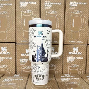May include: A white 40 oz Stanley Quencher H2.0 tumbler featuring a dark blue graphic of a castle, fireworks, a heart, and a character illustration. The tumbler has a large side handle, a white lid, and the text The Flowstate Quencher H2.0.