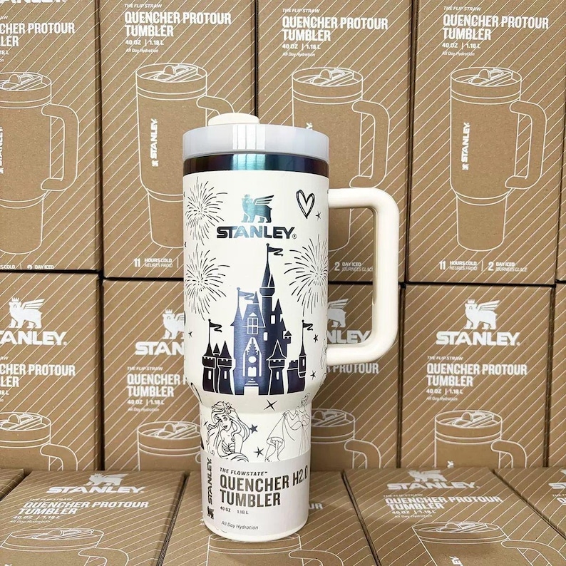 May include: A white 40 oz Stanley Quencher H2.0 tumbler featuring a dark blue graphic of a castle, fireworks, a heart, and a character illustration. The tumbler has a large side handle, a white lid, and the text The Flowstate Quencher H2.0.