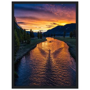 May include: A framed wall art print featuring a landscape at sunset with a river flowing through a valley. The water reflects the vibrant orange and purple sky, while a dark silhouette of a bird with wings spread is visible on the water surface.