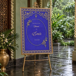 May include: A rectangular sign with a deep blue background and gold floral borders, displayed on a gold metal easel. The sign features the text "WELCOME TO THE Sunnet OF Emir" and the date "12.04.2030" in elegant gold lettering inside an oval.