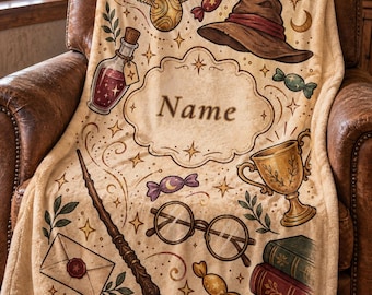 Può includere: Una coperta in pile beige con una cornice decorativa centrale con il testo Name, circondata da illustrazioni di una palla dorata alata, un cappello a punta marrone, una pozione, una bacchetta, occhiali tondi, un trofeo dorato e caramelle.
